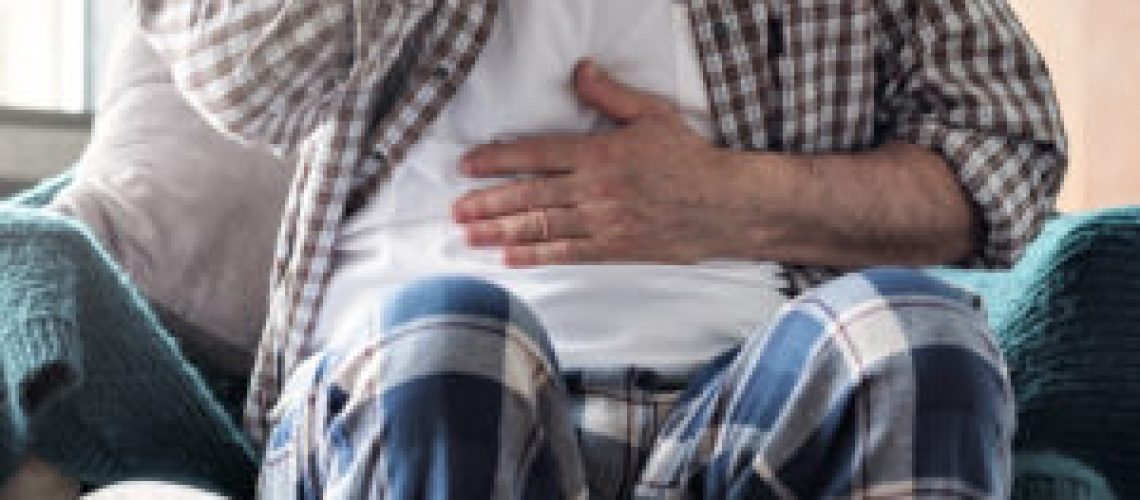 Man with abdominal pain, stomach ache sitting in the living room. No face view