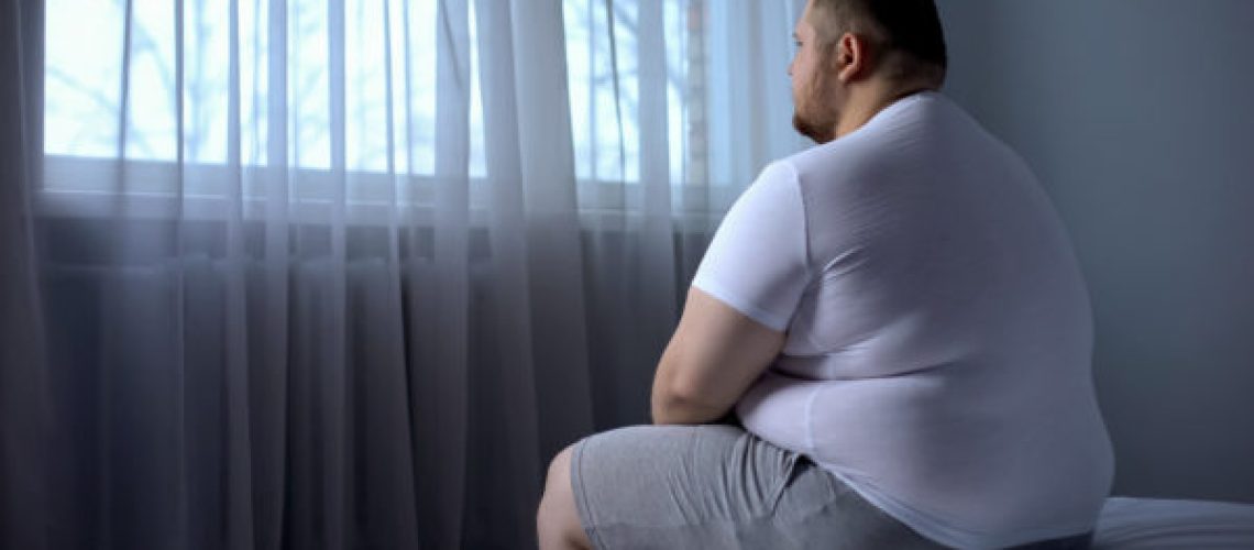 Sad heavy man sitting on bed at home, health problem, depression, insecurities